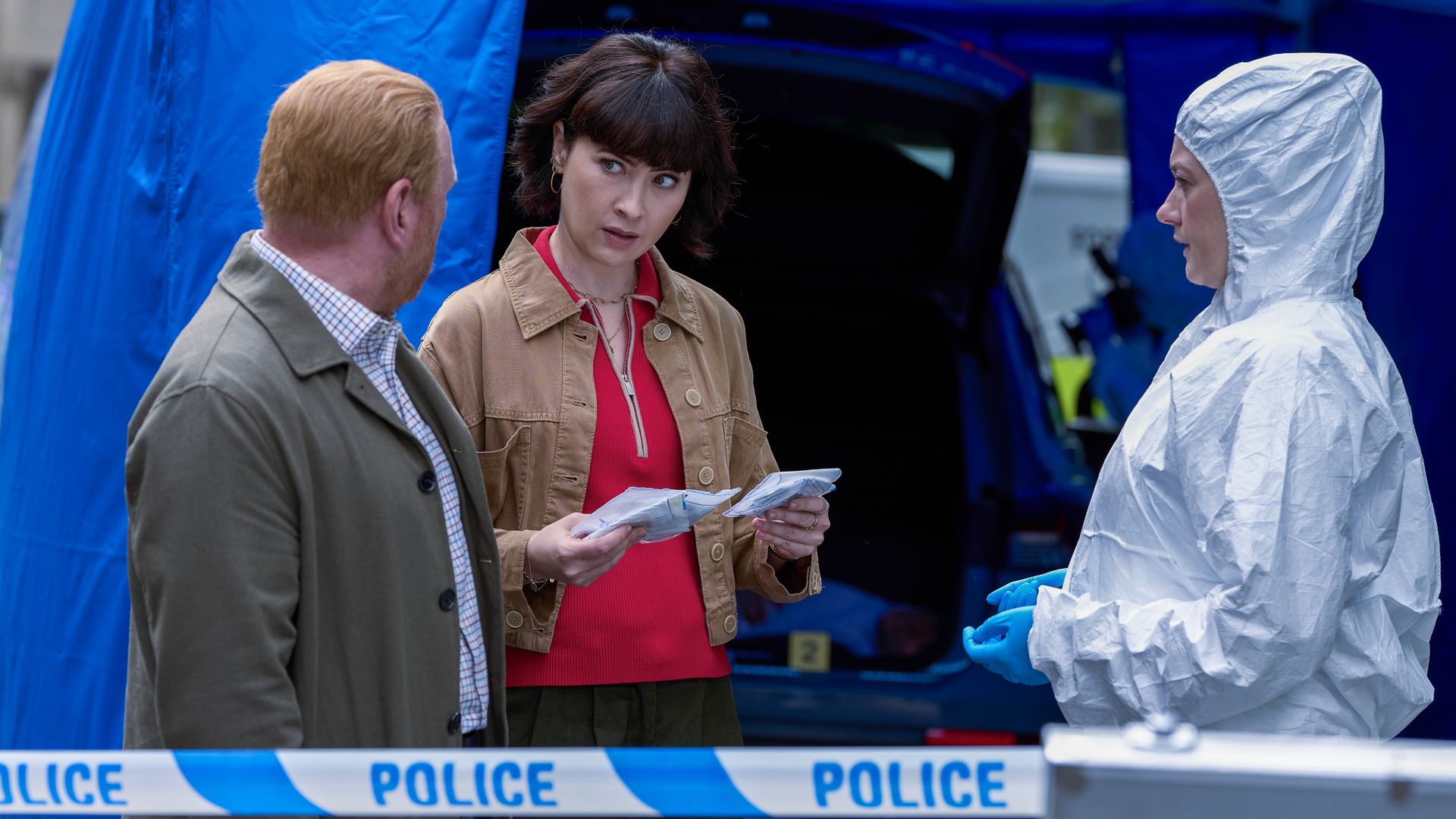 police officers standing next to woman in forensic suit in front of blue police tape