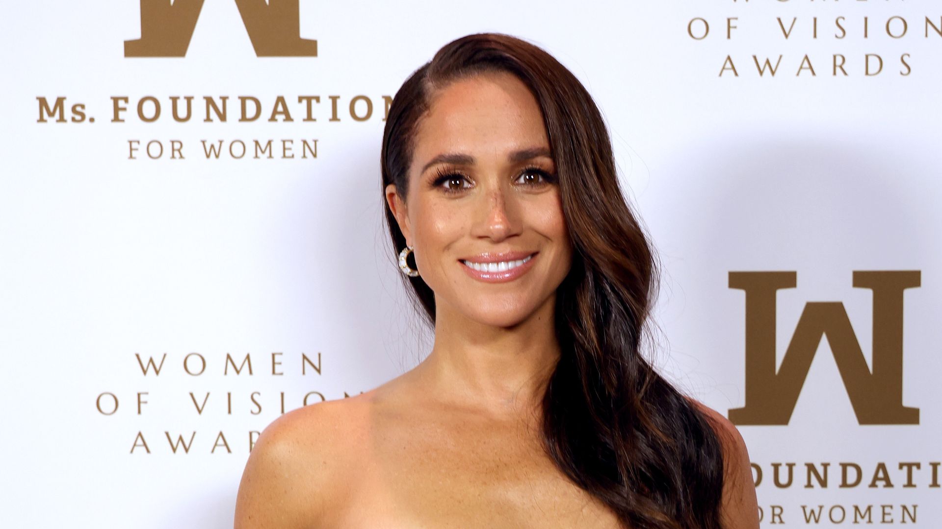 Meghan Markle smiling, wearing a gold dress at the Women of Vision Awards