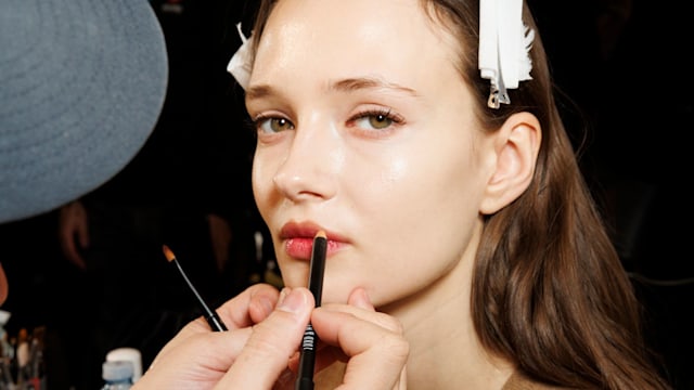 A makeup artist works on a model  backstage