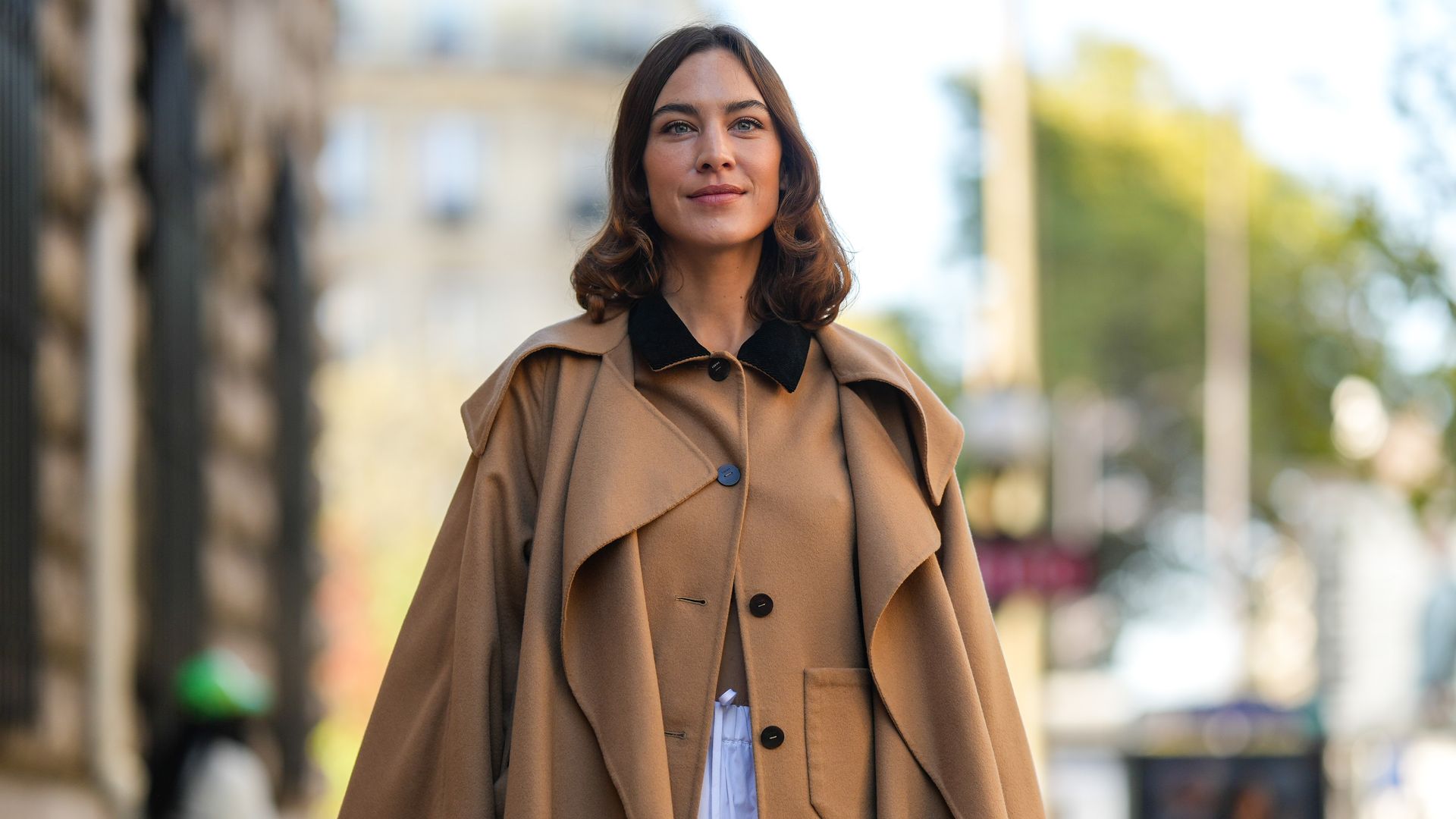 PARIS, FRANCE - SEPTEMBER 30: Alexa Cheung wears a beige buttoned / black collar jacket, a beige long trench coat, a white ruffled midi skirt, a black shiny leather handbag, outside Loewe, during Paris Fashion Week - Womenswear Spring/Summer 2023, on Sept