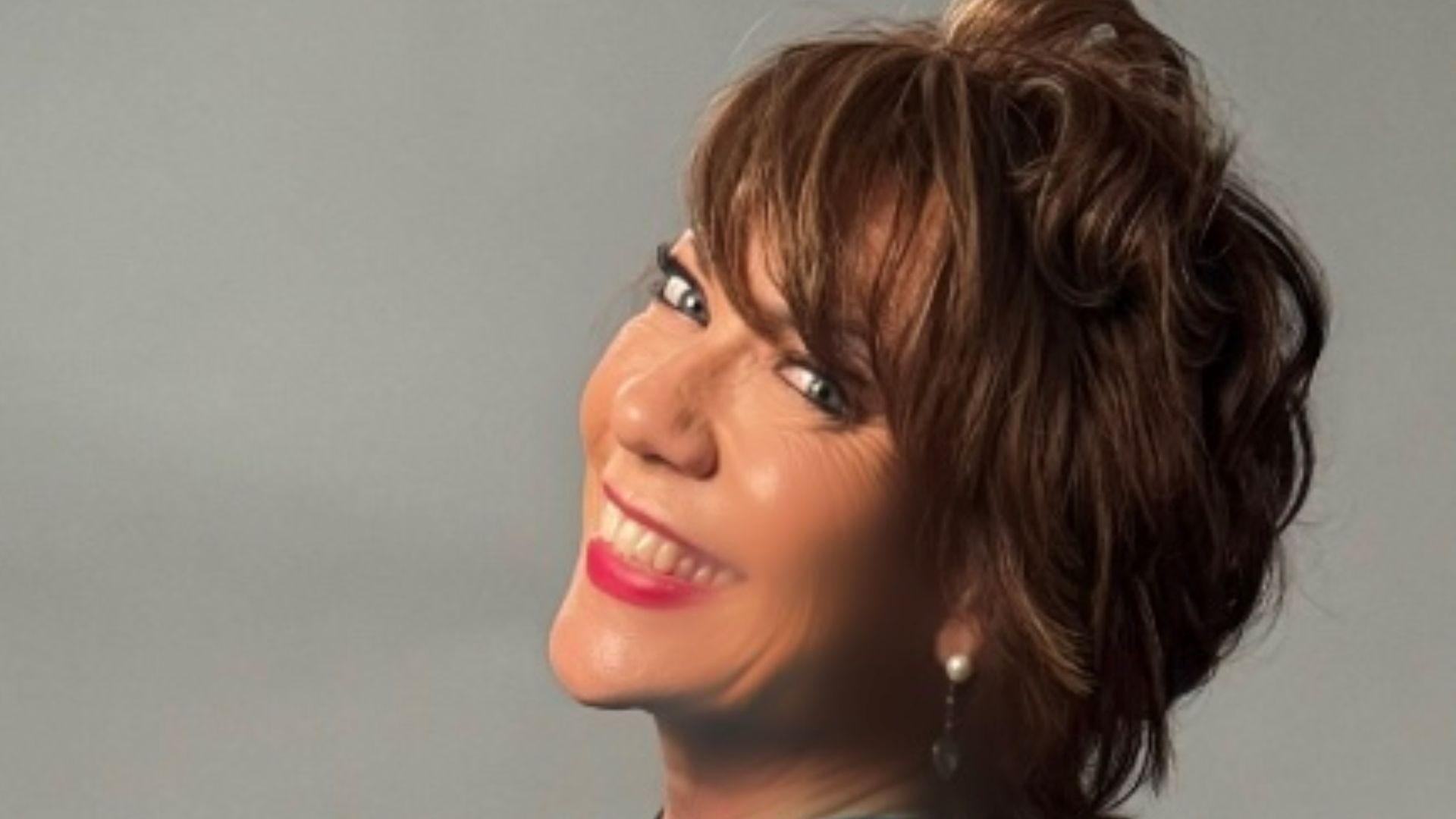 author kathy lette smiling over her shoulder in a blue printed top