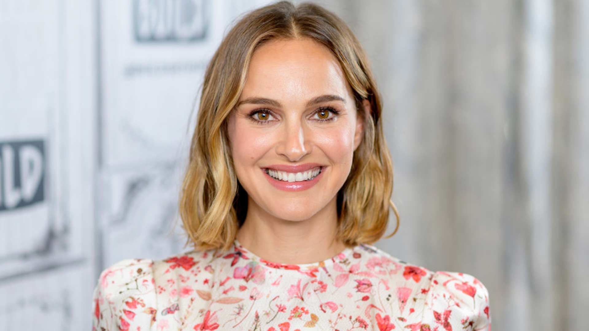 Natalie Portman smiling in a white and pink floral dress
