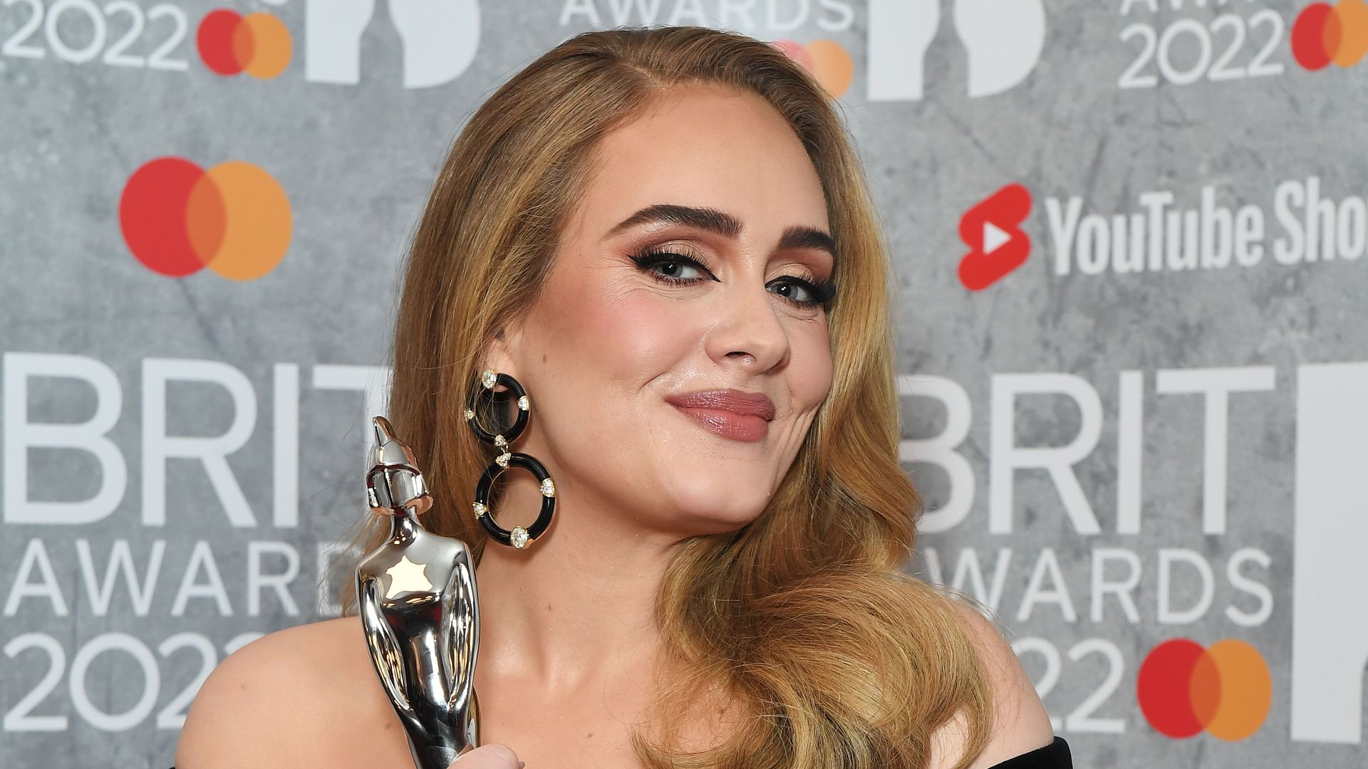 Adele holding awards in a black dress