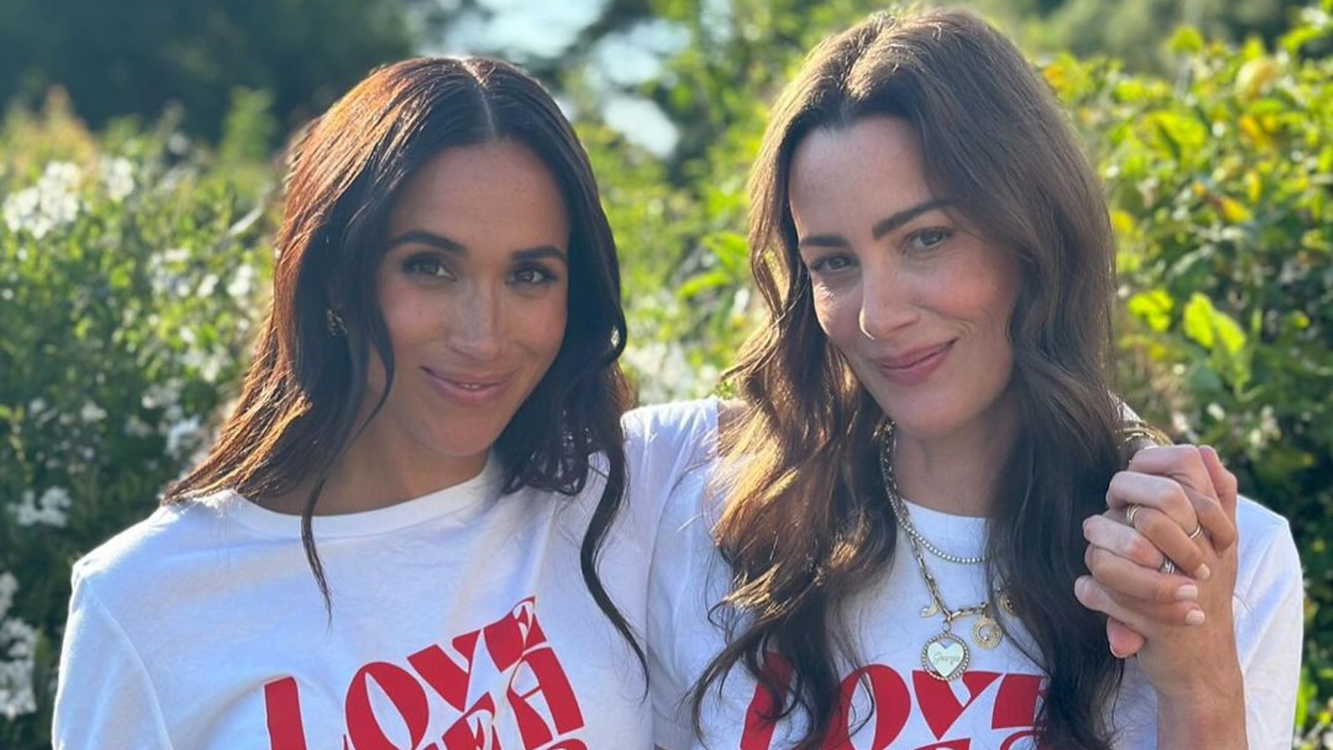 Meghan Markle posing with a friend wearing a t-shirt saying 'love like a mother'