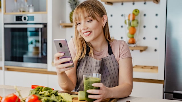 Young woman is in the kitchen and she is using mobile phone