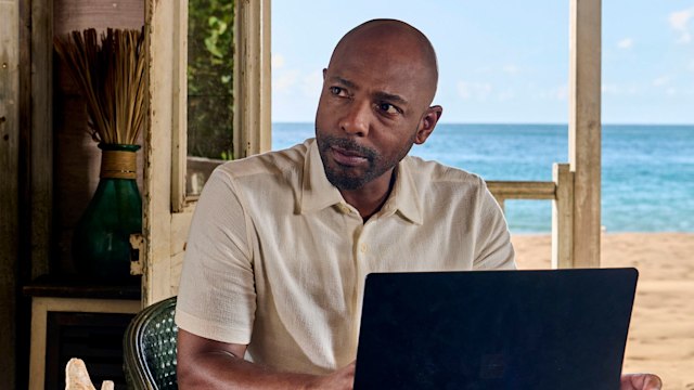 Man sitting at desk with laptop in front of beach background