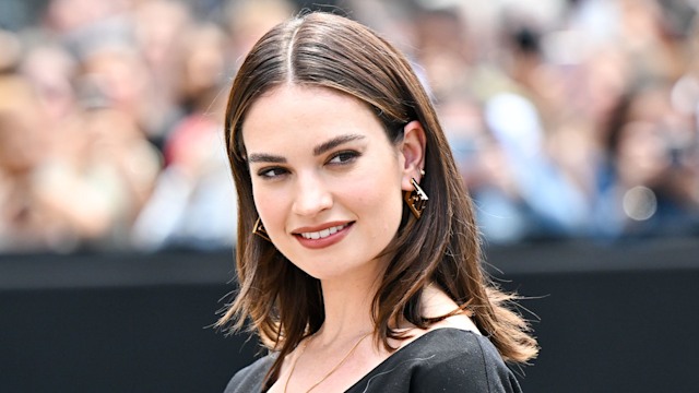 Lily James smiling, wearing a black dress and gold jewellery at Paris Fashion Week 