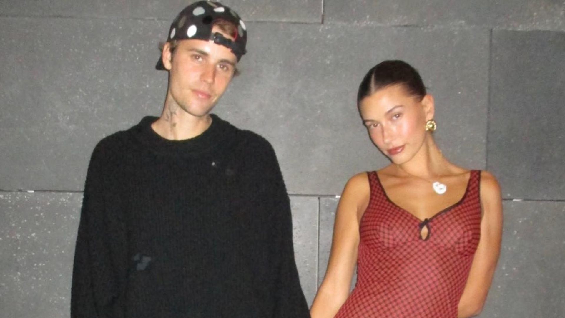 justin and hailey bieber standing in front of brick wall holding hands