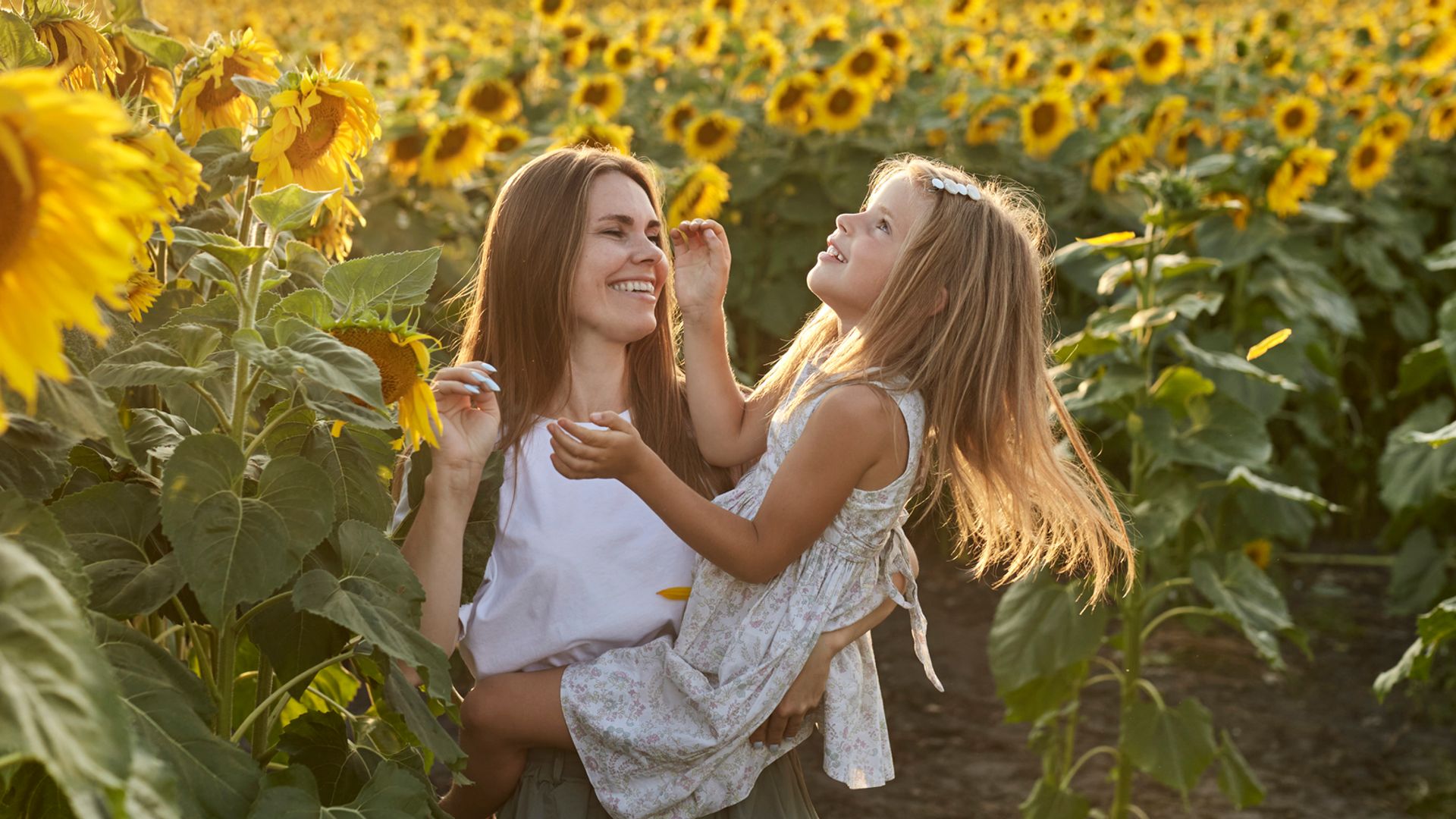 Happy mother carrying daughter in a sunflower field