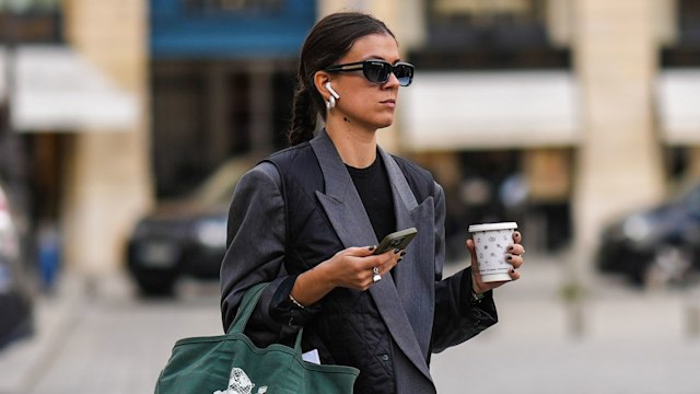 PARIS, FRANCE - SEPTEMBER 29: A guest wears black sunglasses, a white pearl earrings, a black t-shirt, a gray oversized blazer jacket, a black quilted sleeveless gilet, dark gray suit pants, a dark green with embroidered white print pattern handbag, black shiny leather nailed / studded with brown wood block heels shoes , outside Schiaparelli, during Paris Fashion Week - Womenswear Spring/Summer 2023, on September 29, 2022 in Paris, France. (Photo by Edward Berthelot/Getty Images)