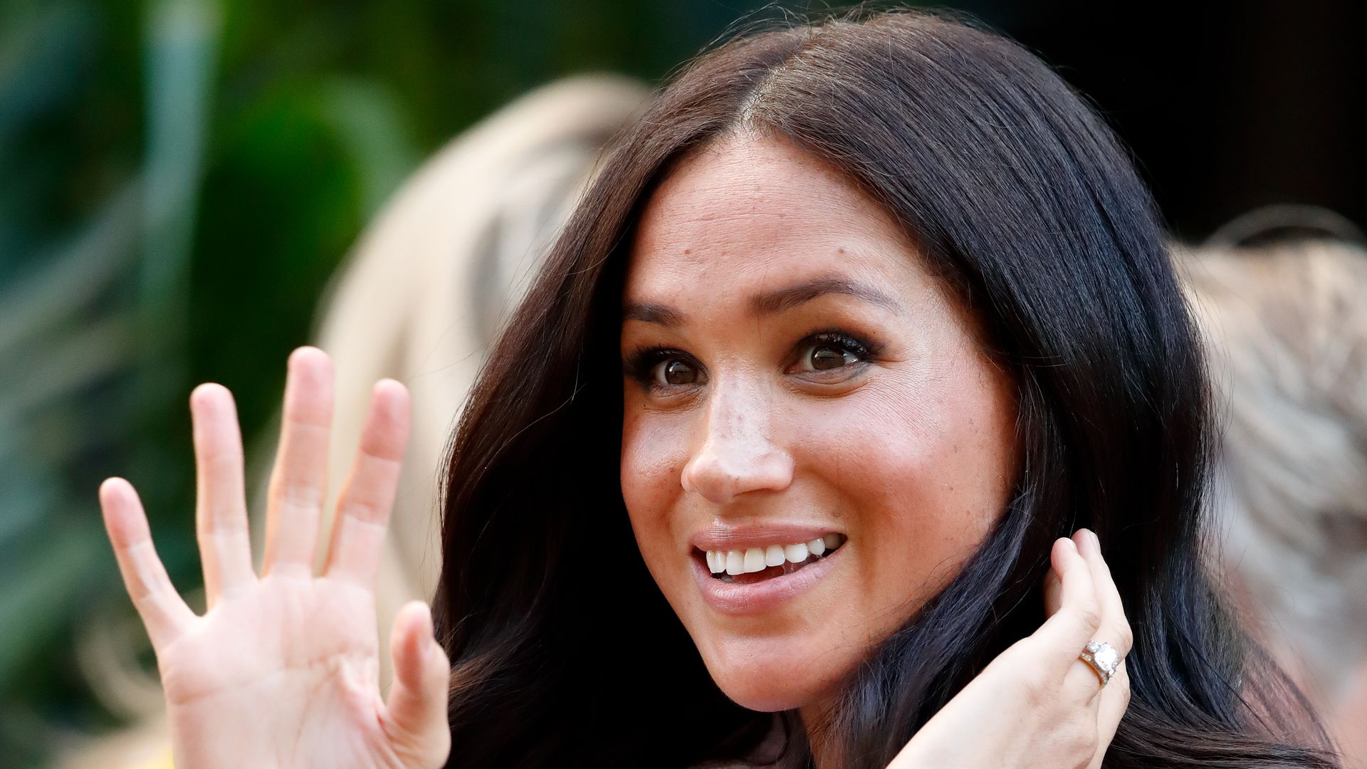 Meghan, Duchess of Sussex with hand up waving in white shirt