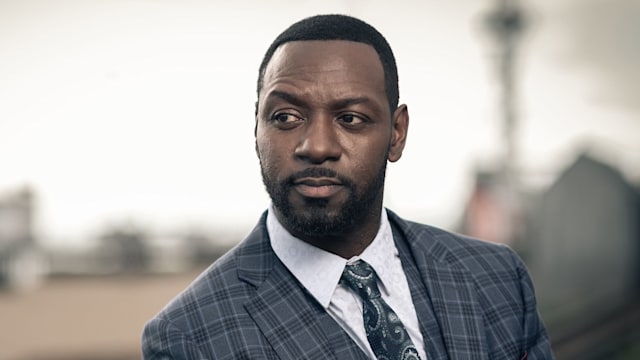 Man in grey suit standing against blurred background