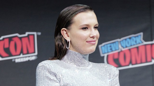 Millie Bobbie Brown on directors chair in silver outfit