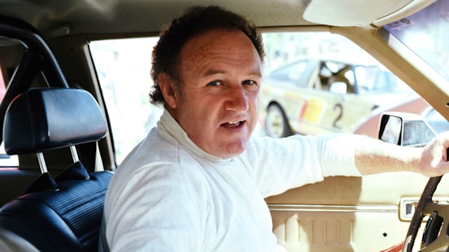 gene hackman sitting in a car looking at camera