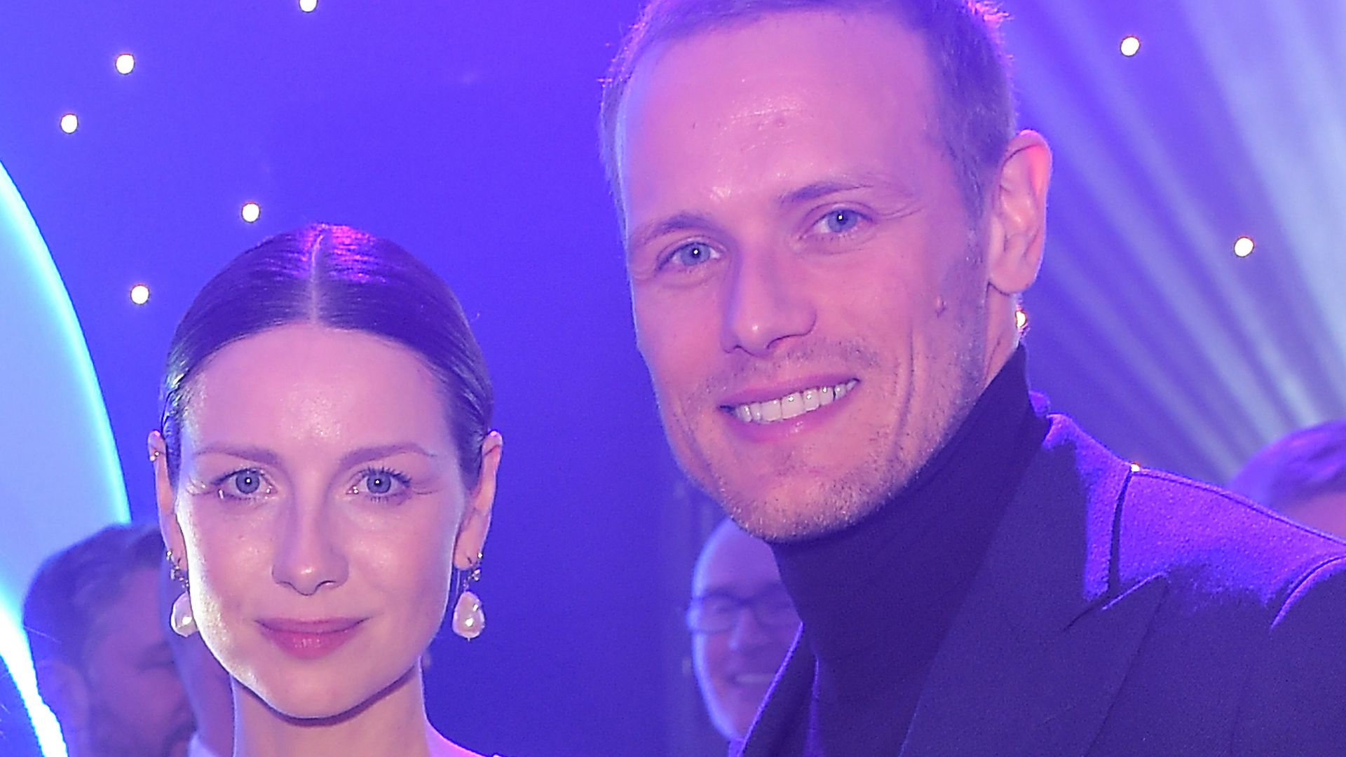 Sam Heughan and Caitriona Balfe smiling at the camera
