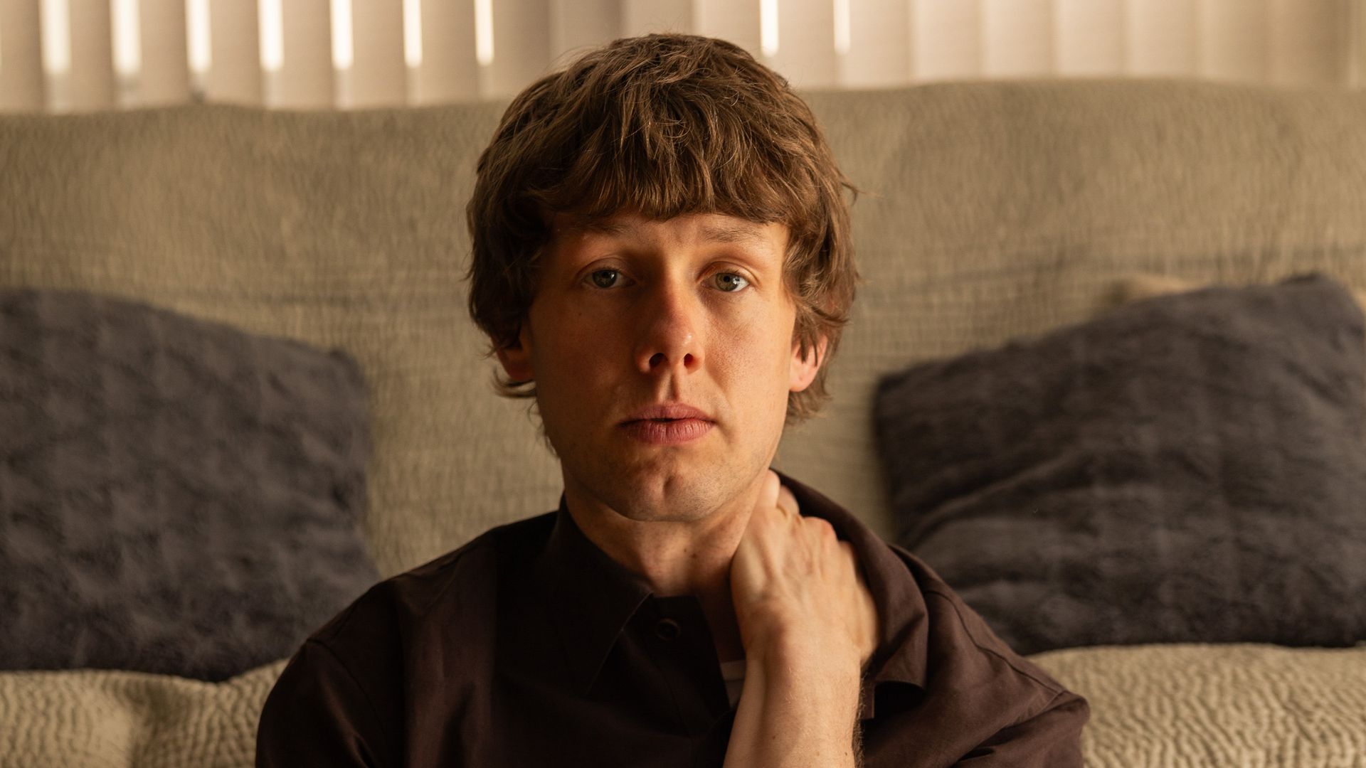 Josh Finan sitting by a sofa in a scene from Waiting for the Out