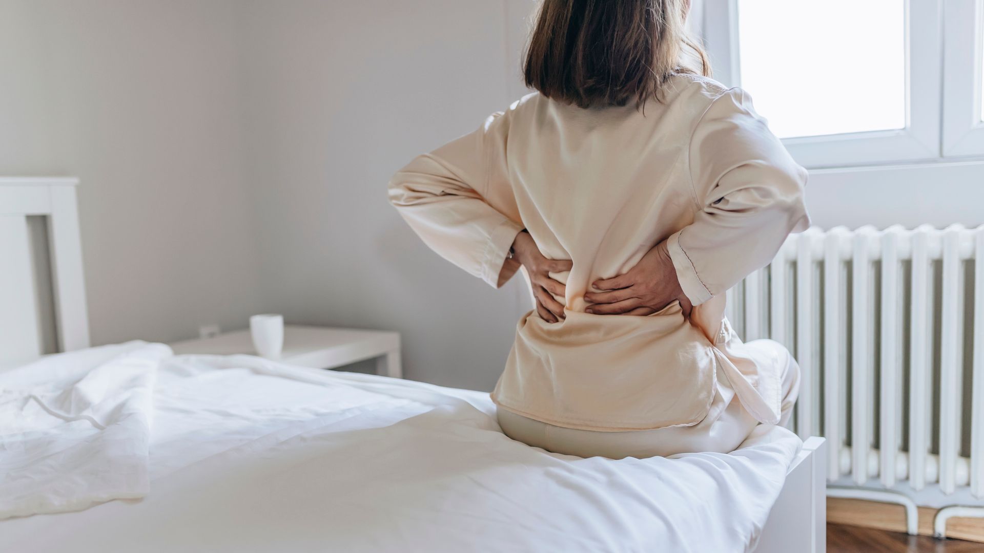 Cropped Image of Senior Woman Suffering From Backache in Morning Sitting on Bed, Panorama With Free Space. Lower Back Pain in Elderly Person. Woman Feels Back Pain Massaging Aching Muscles. Mature Woman Feeling Morning Discomfort in Aching Back in the Bedroom.