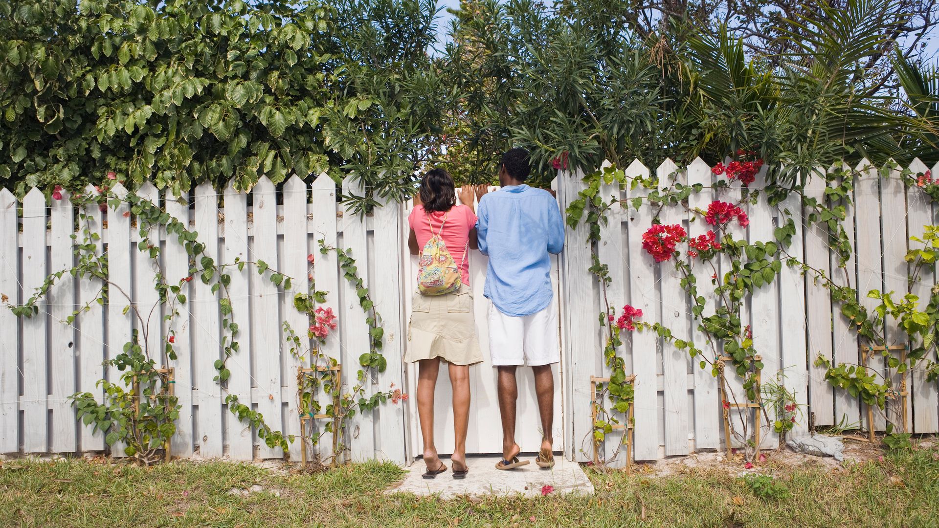 Young couple looking over white picket fence, rear view