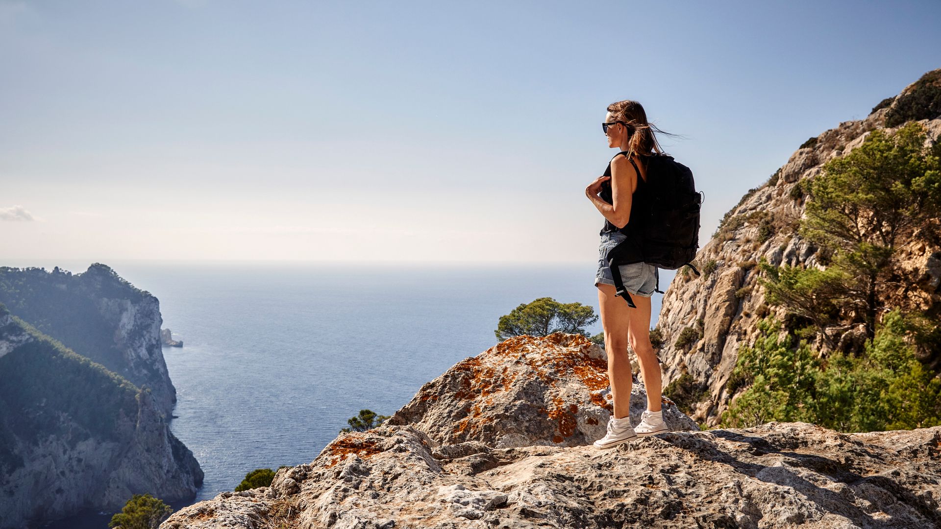 A young woman on a Summer hike in nature in Ibiza with cliffs and the sea in the background.