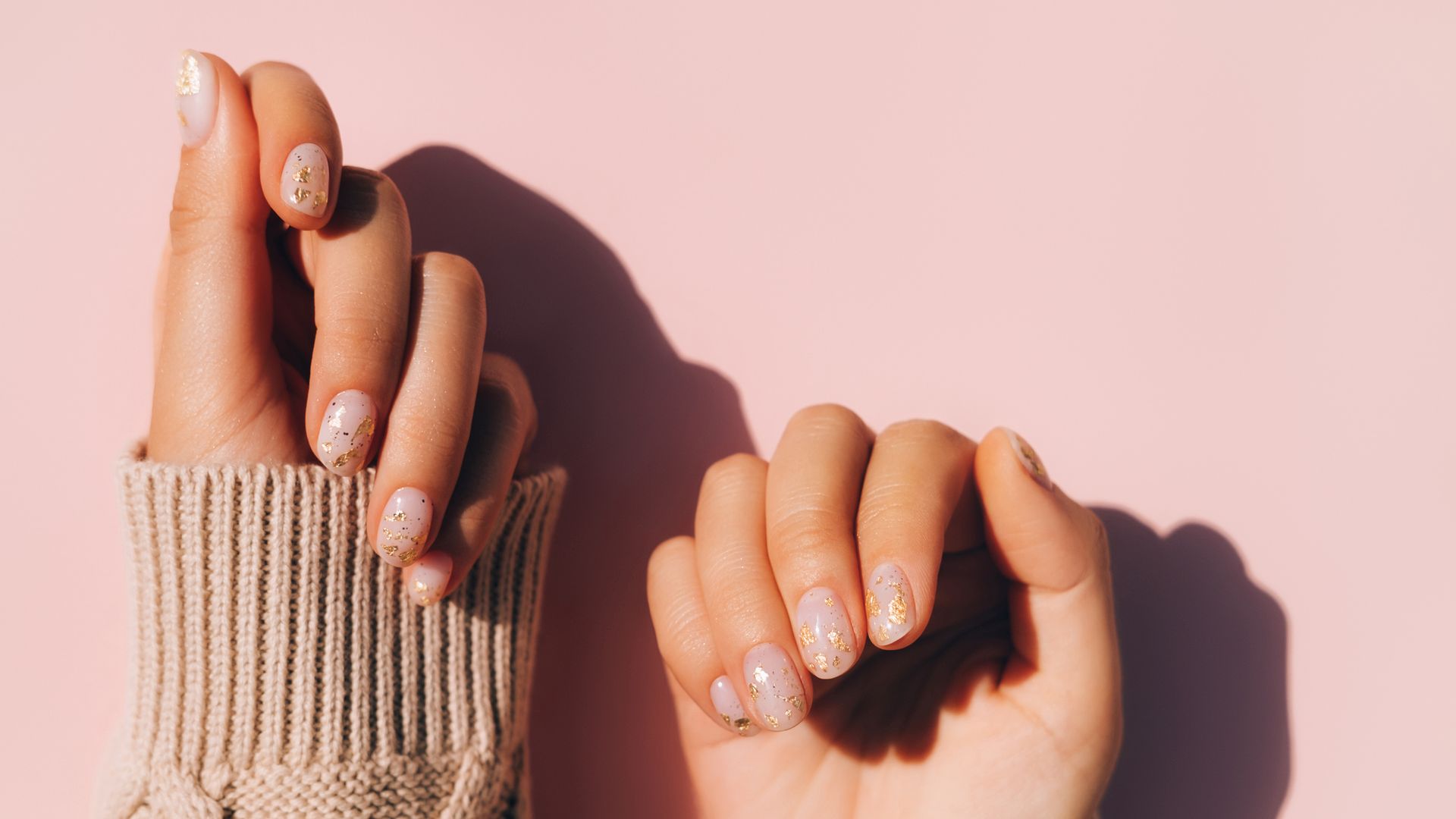 Glowing hands in sweater with knitted sleeves and with nude color manicure with gold particles on pink table
