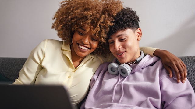 woman sitting with teenage son on the sofa at home using a laptop 