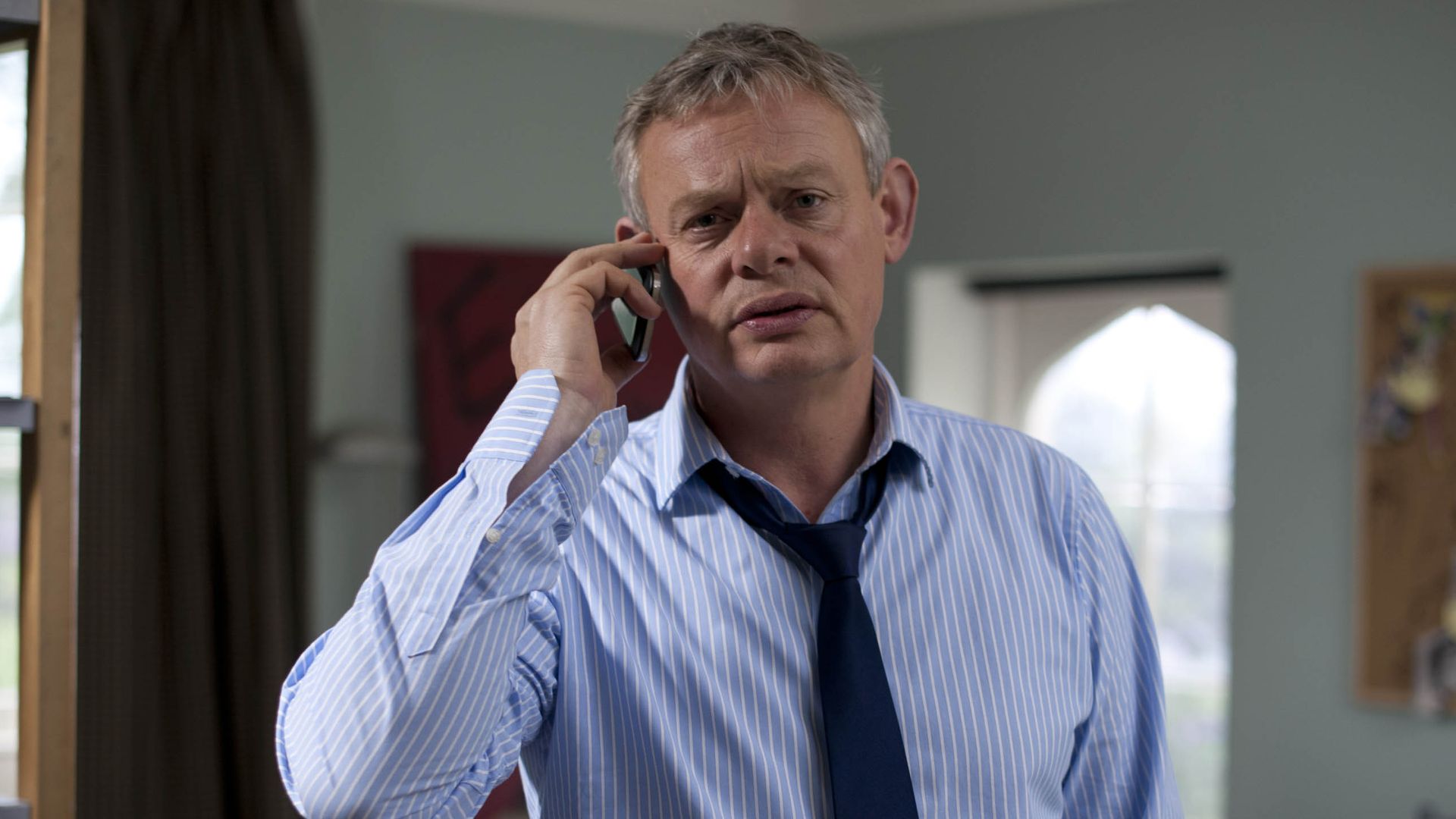 man in shirt and tie standing in bedroom holding mobile phone 