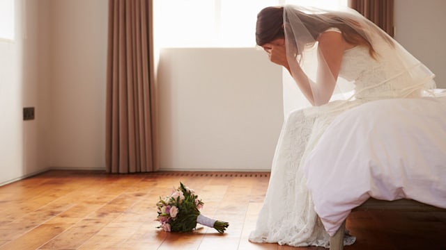 Bride sitting on the bed with her head in her hands and her flowers on the floor
