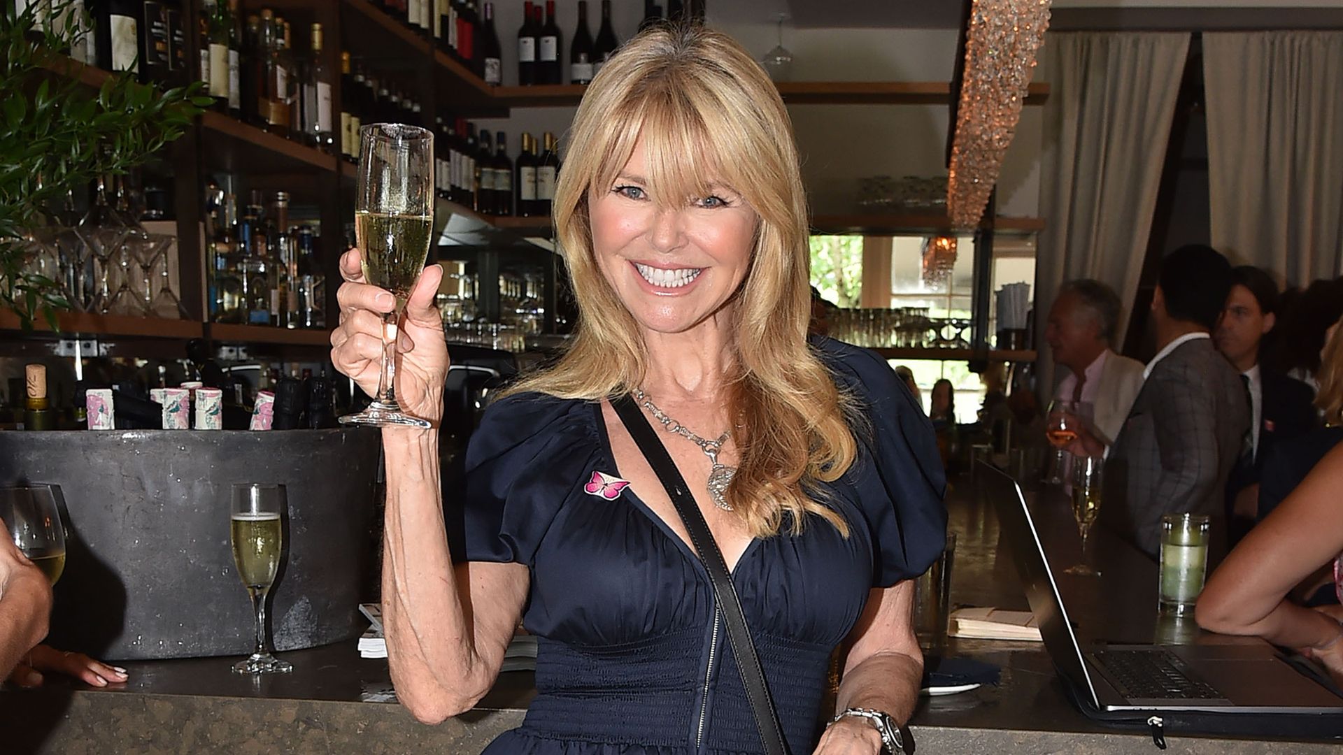 Christie Brinkley in black dress holding a wine glass