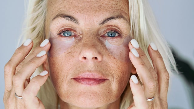 How to cover up age spots - and look 10 years younger - Older woman applying on her face hydrogel under-eye recovery patches. Do morning routine, to reduce puffiness. Skincare treatments usage, beauty routine concept