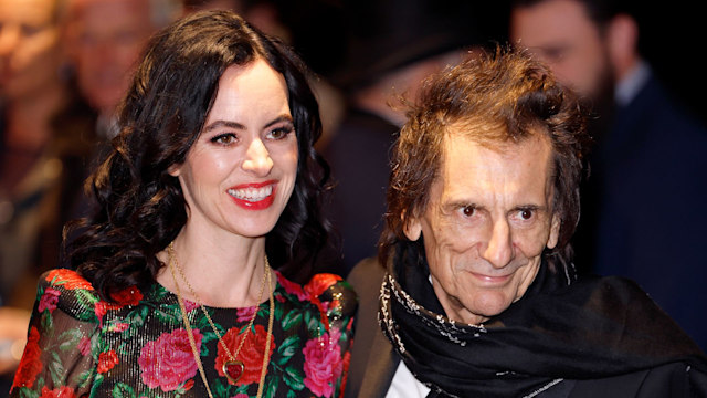 Ronnie Wood and wife Sally - Sally wears a floral dress and Rod wears a black suit and scarf