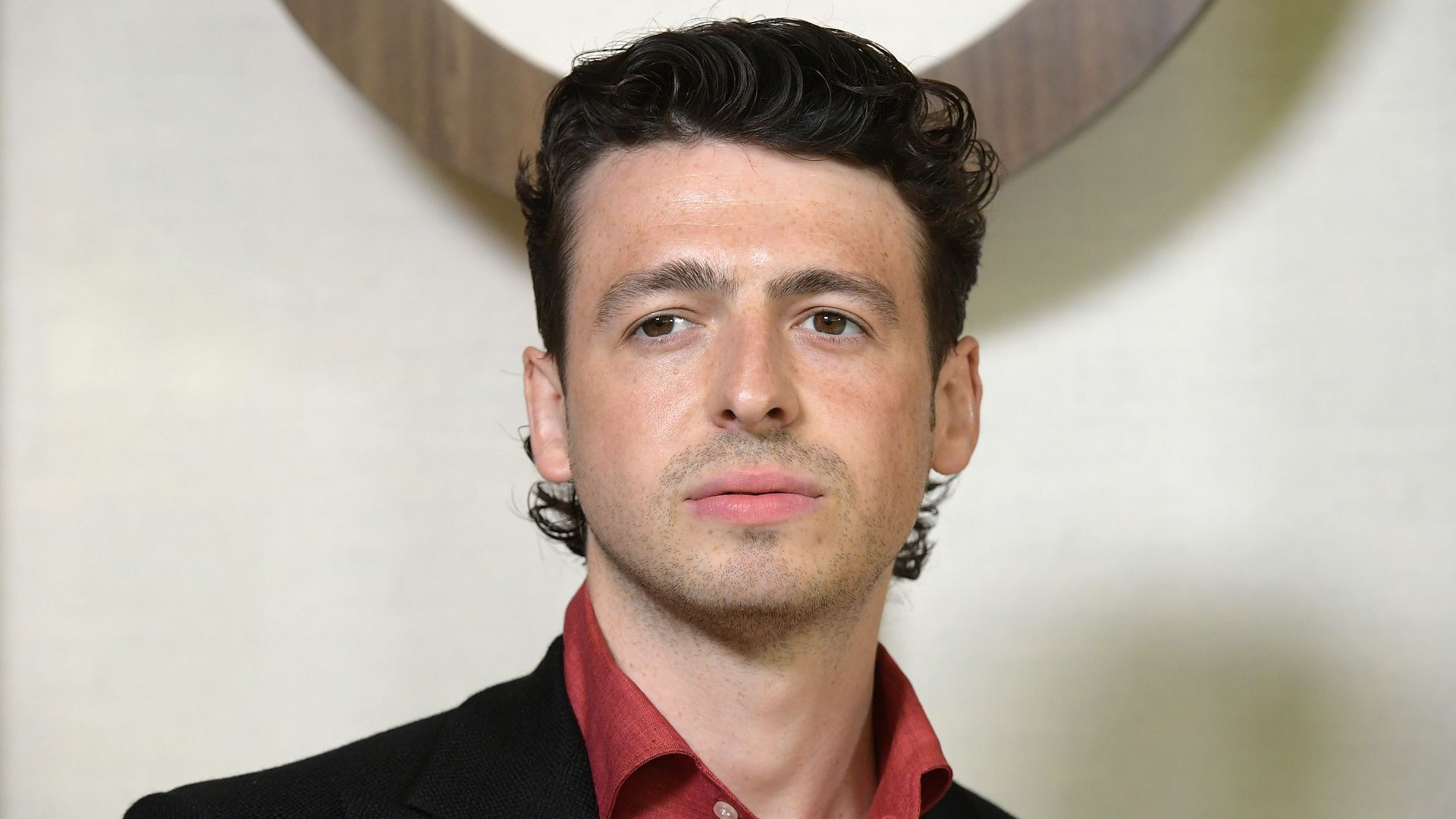 Anthony Boyle shoulders up in red shirt and black blazer