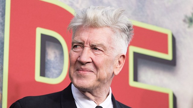 David Lynch in a black suit in front of red lettering