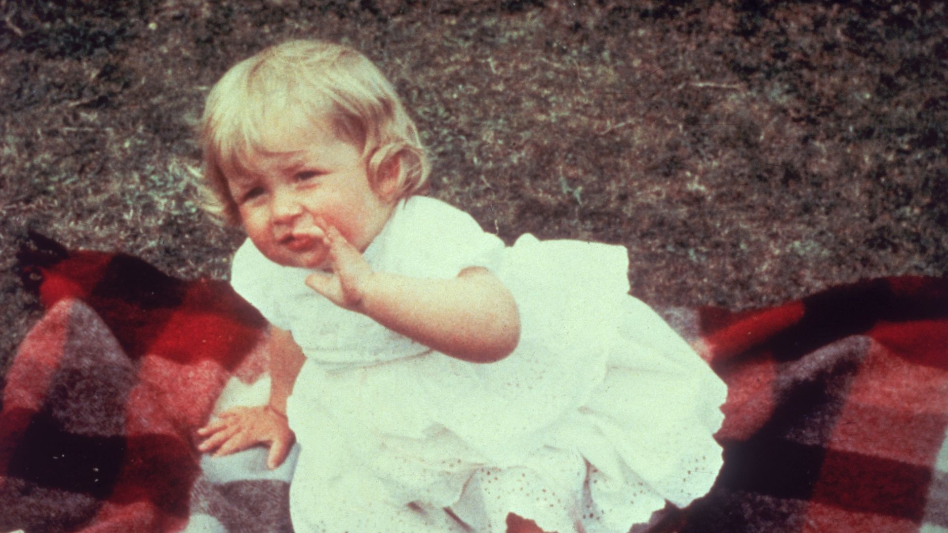 A baby Princess Diana in a white dress on a blanket