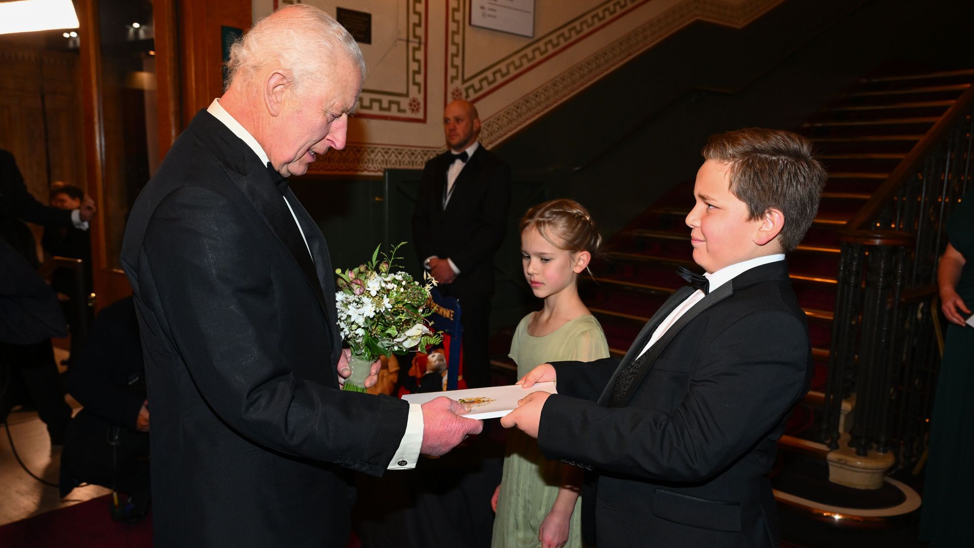 King Charles being given a programme by a male child in a suit