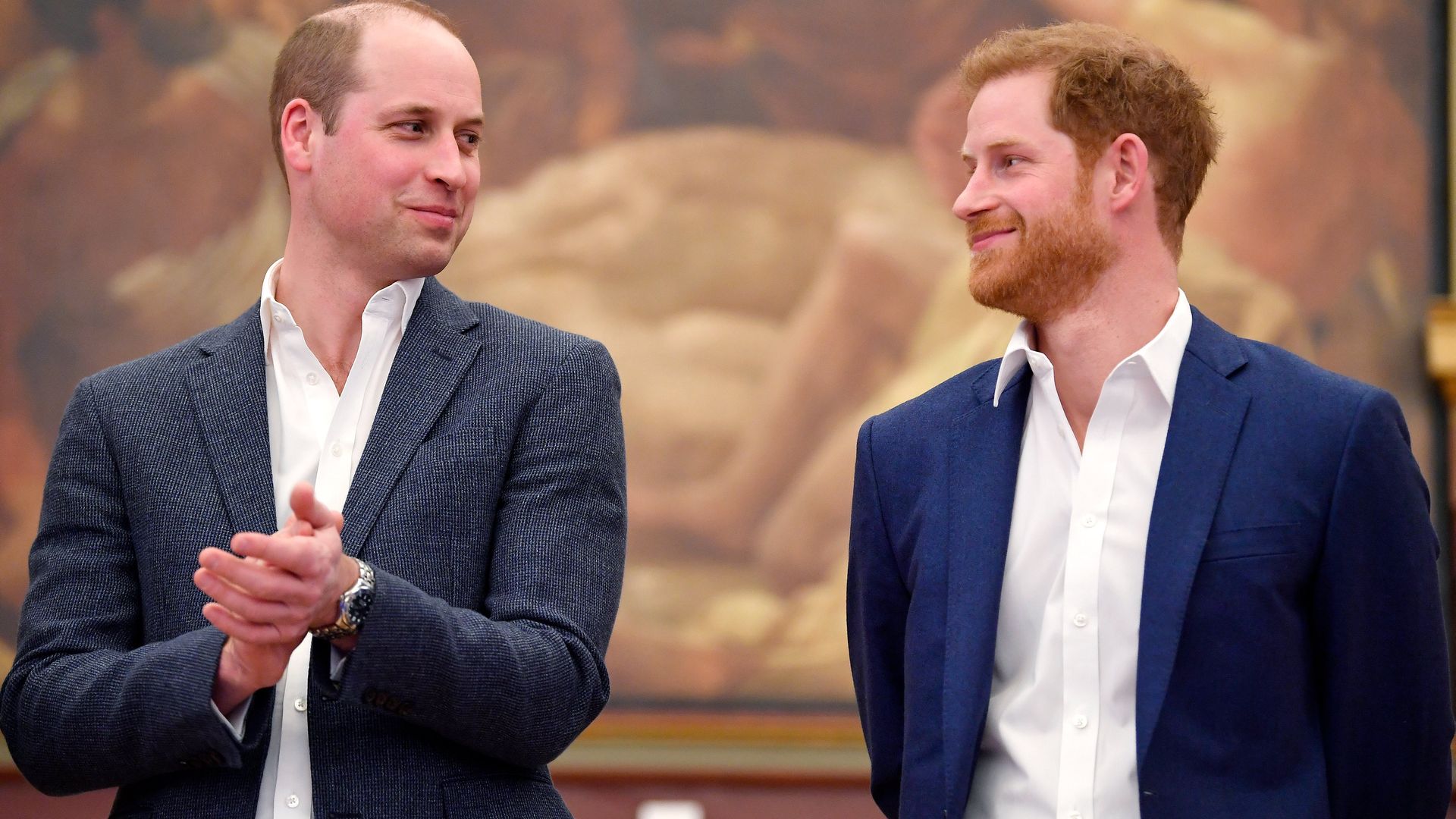 Prince William and Prince Harry smiling at eachother in suit jackets and shirts