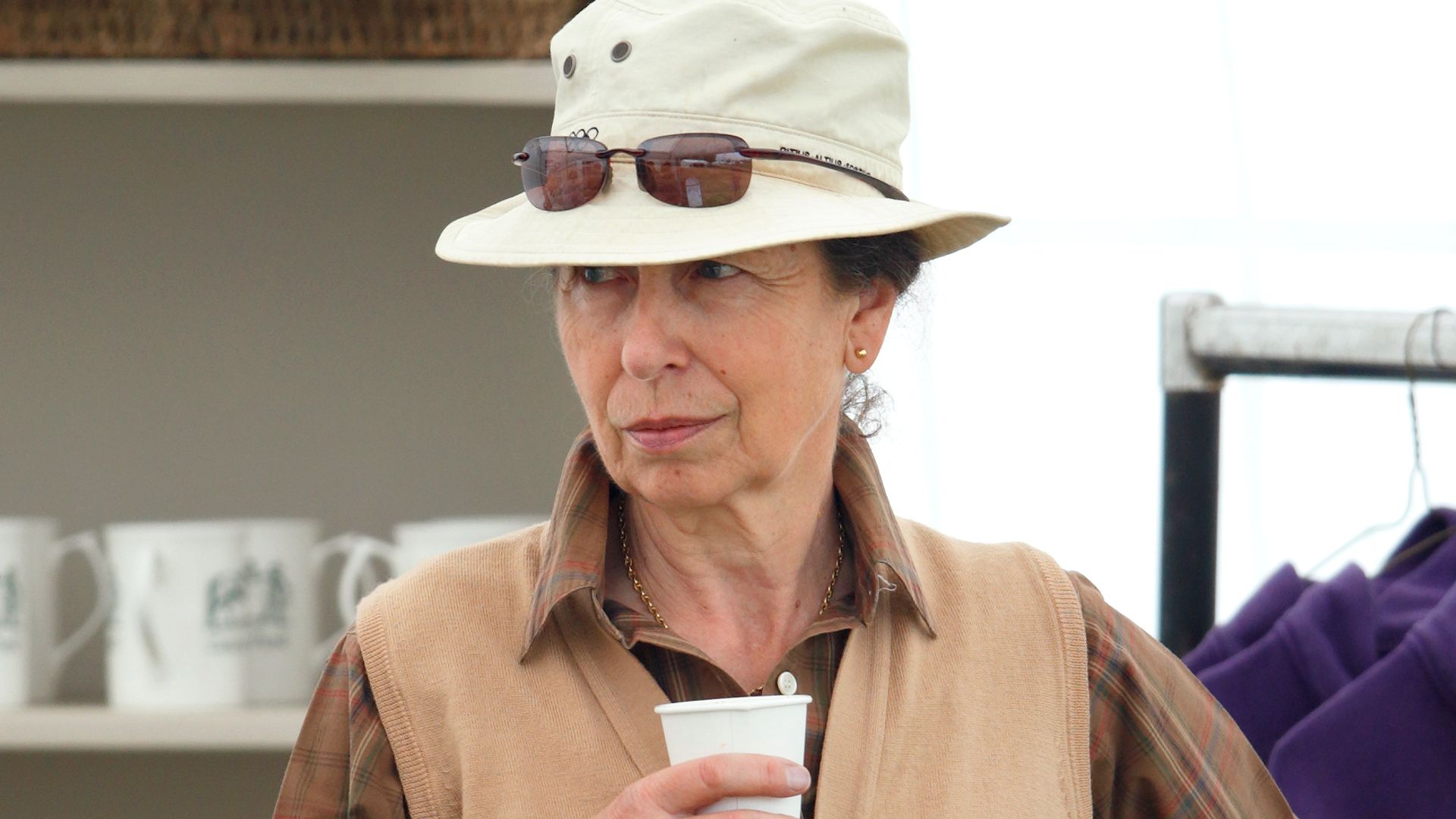 Princess Anne holding a drink while wearing a hat and sunglasses