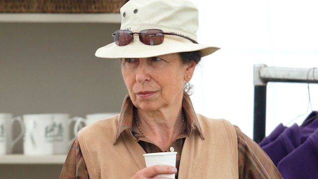 Princess Anne holding a drink while wearing a hat and sunglasses