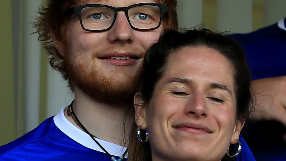 Ed Sheeran e Cherry Seaborn em um jogo de futebol, ela está descansando a cabeça no ombro dele