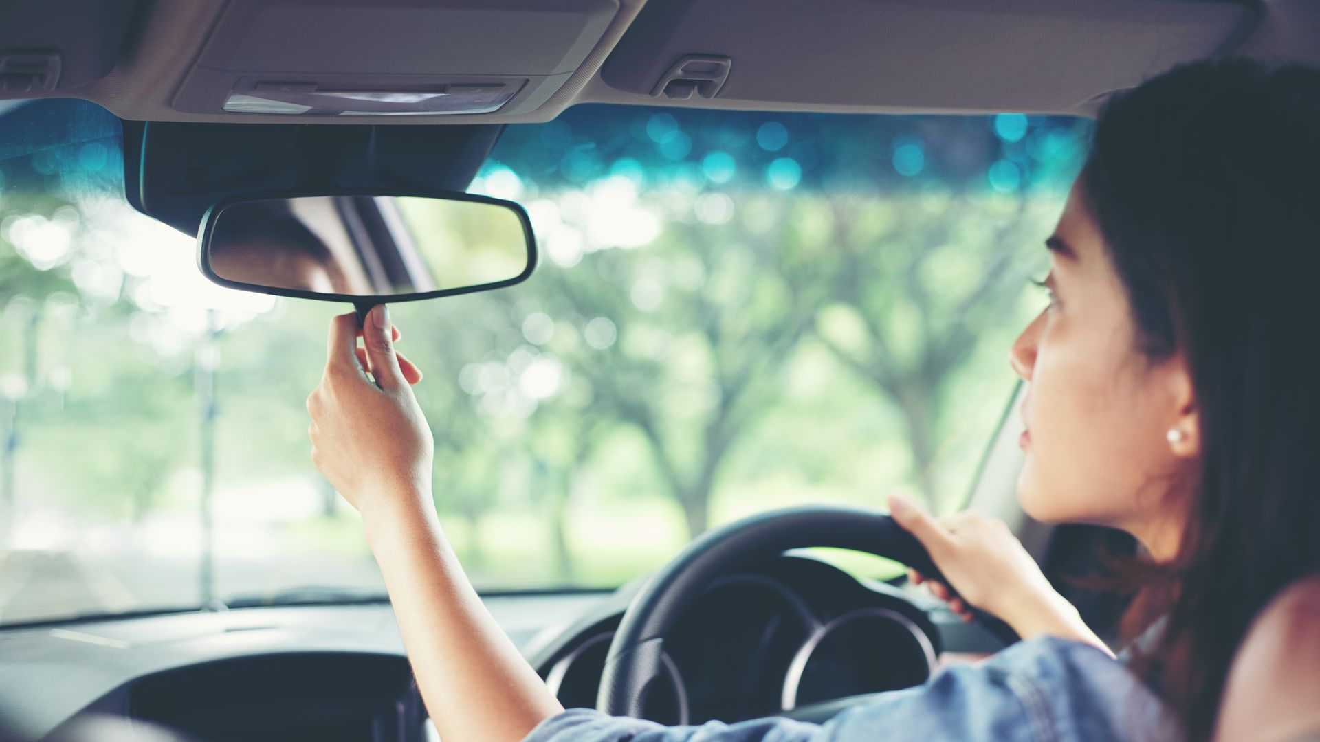Woman adjusting rear view mirror driving in car