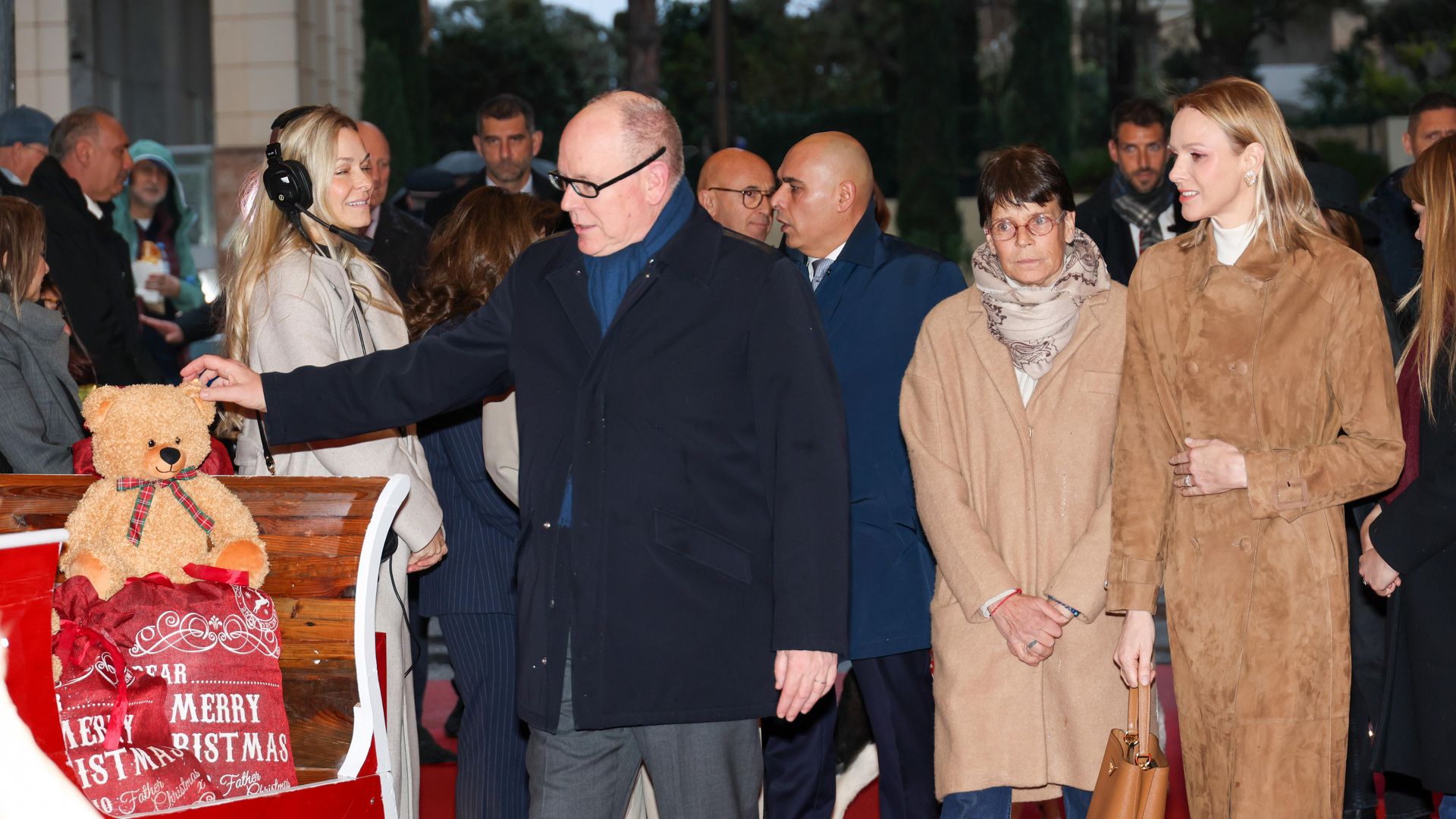 Prince Albert touching a teddy bear as Princess Stephanie and Princess Charlene look on
