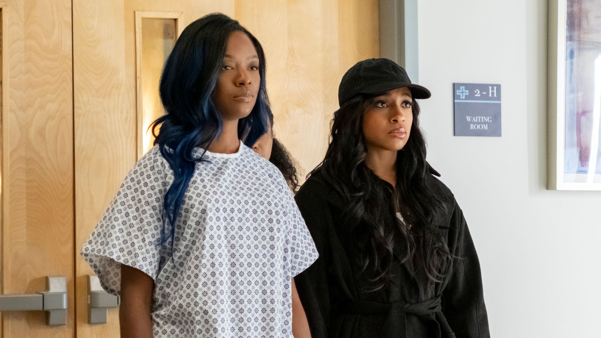 woman in hospital gown standing next to woman in black in hospital ward