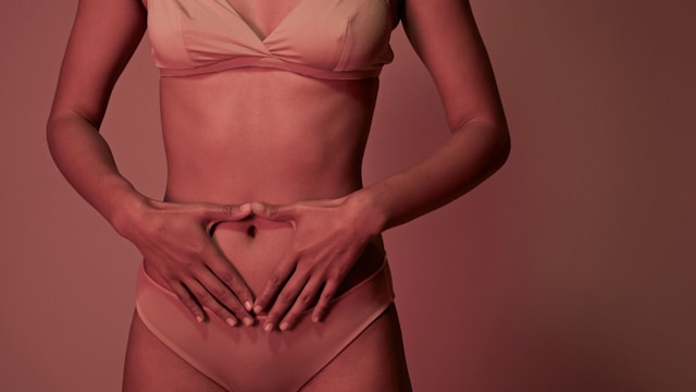 Young woman making a heart on her stomach while wearing underwear, photographed in studio with coloured lights
