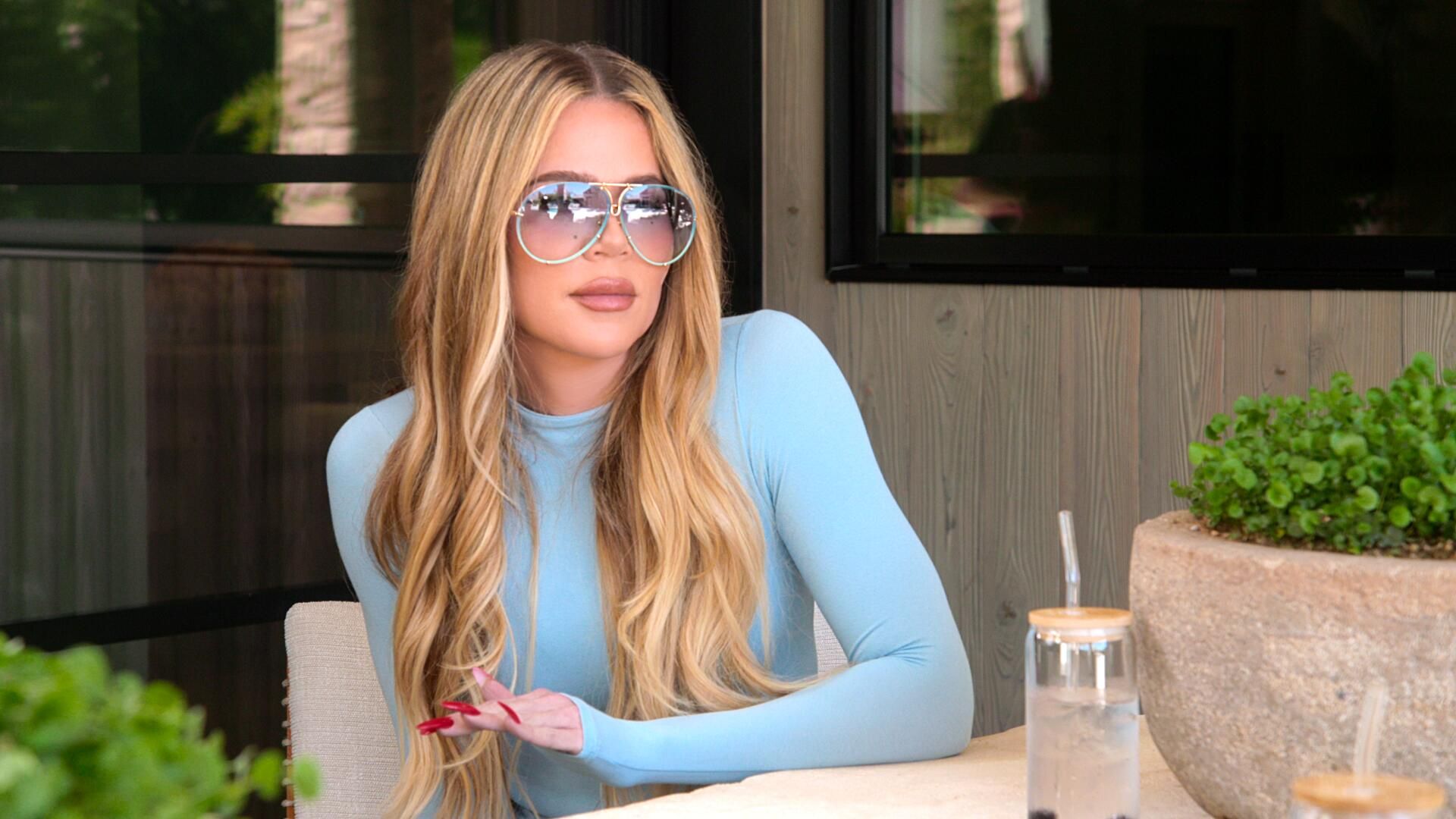 Khloe Kardashian sits at an outdoor dining table 