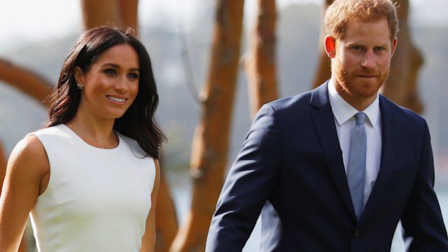 Meghan Markle in a white dress holding hands with Prince Harry