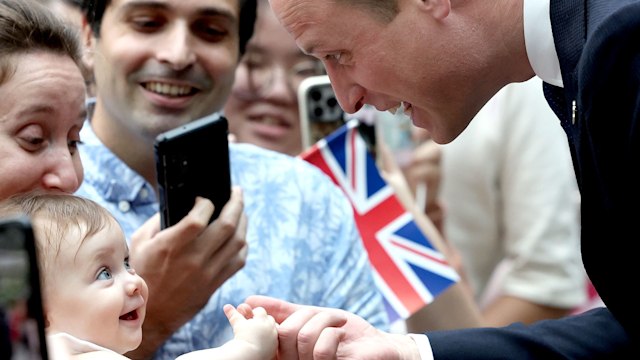 8 month old Albane Costa holds the finger of Prince William, Prince of Wales 