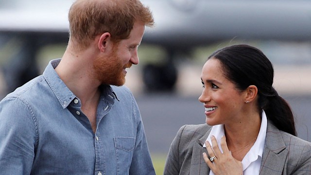 Prince Harry talking to Meghan Markle as they walk outside at an airport