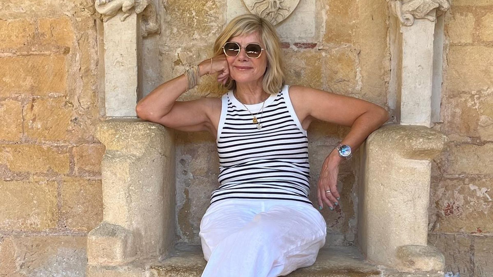 woman in a striped top and white trousers sitting on a stone throne