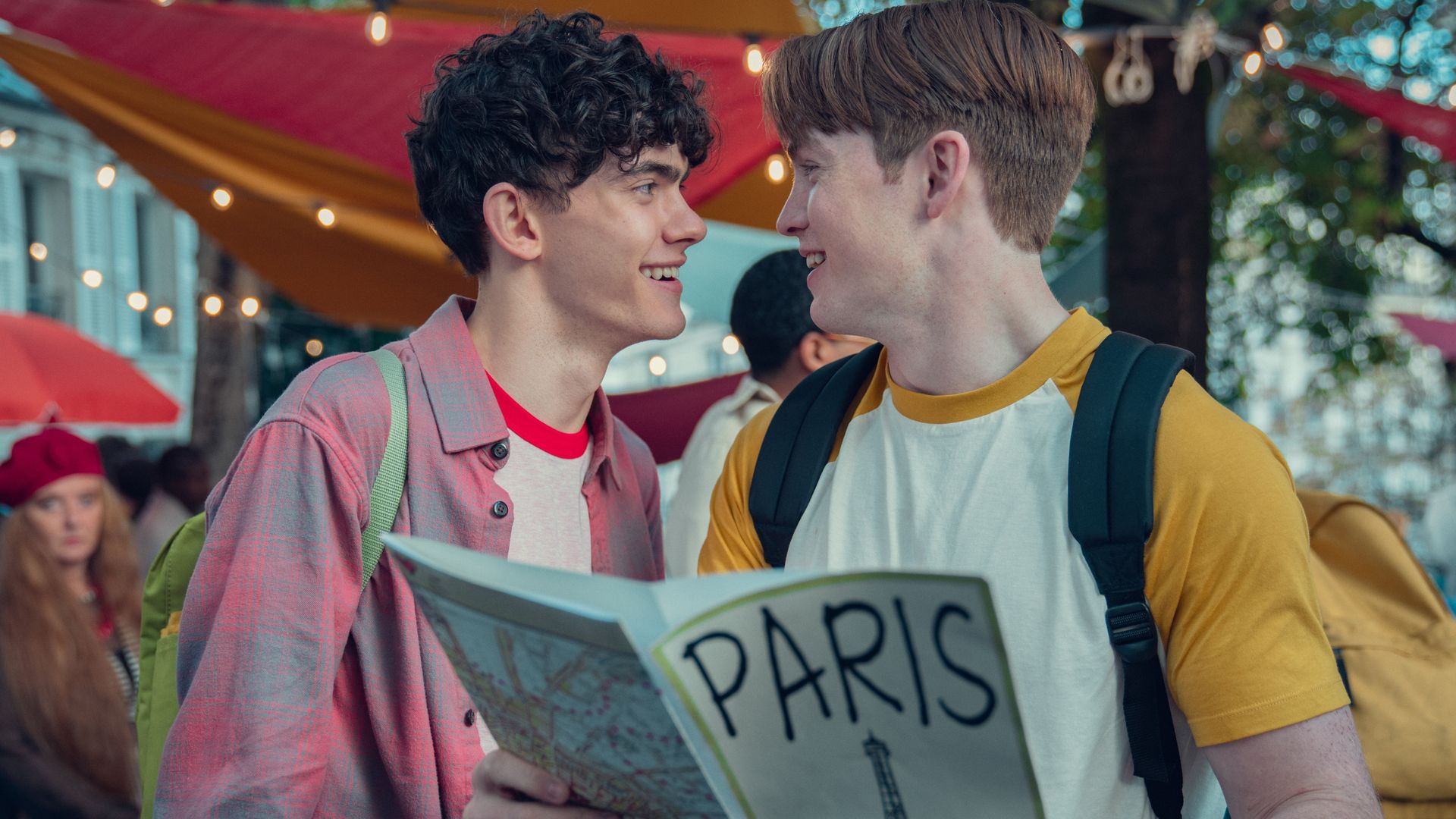 Charlie and Nick grinning at each other, Nick is holding a map of Paris