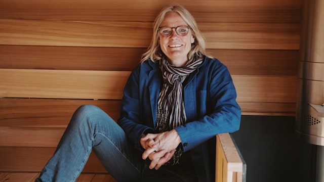 Woman in jumper, jeans and a scarf inside a saunca