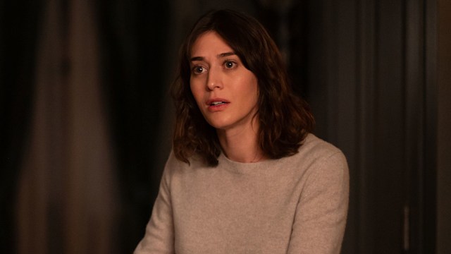 Brunette woman in grey jumper standing next to table